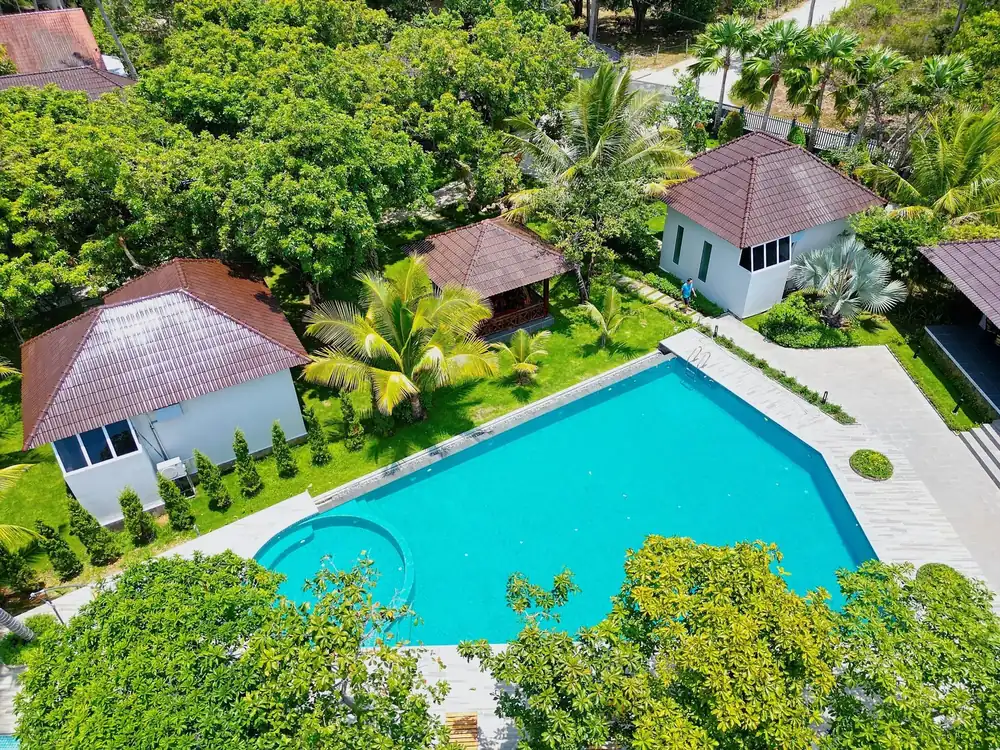 Aerial view of small red-roofed cottages around a swimming pool, surrounded by dense trees